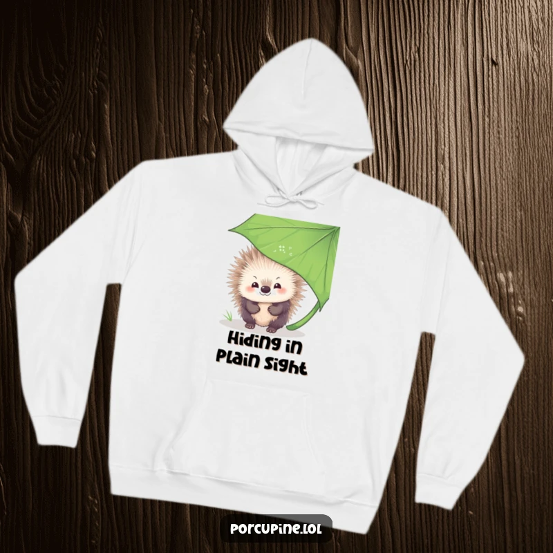 Funny Hoodie showcasing a porcupine with a bashful smile, discreetly peeking from behind a large, verdant leaf, exuding sweet shyness.